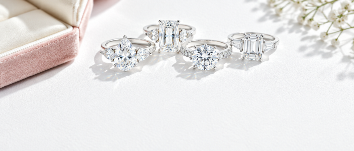 Moissanite engagement rings on white linen beside a blush ring box